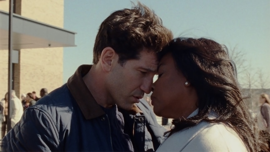 An intimate close-up of a middle-aged white man and a middle-aged black woman, touching their noses together.