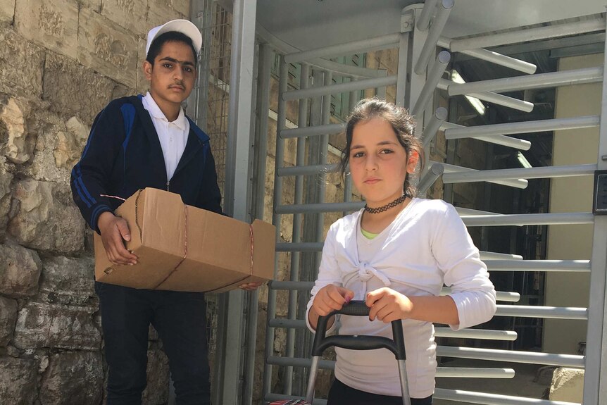 Ameer, 16, carries a large box of tomatoes near the entrance to a checkpoint in downtown Hebron.