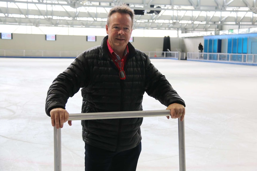 A man stands on an ice rink, holding a metal frame.