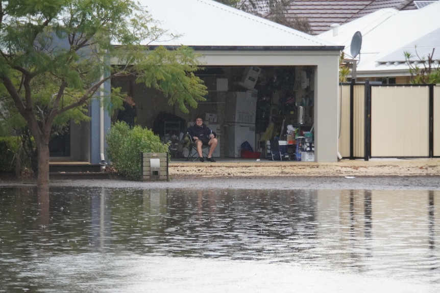 A flooded suburban street with a resident watching from a garage. 
