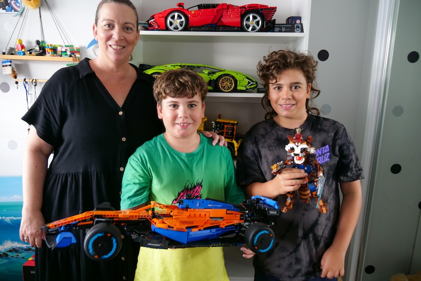 A woman stands with her sons holding Lego builds
