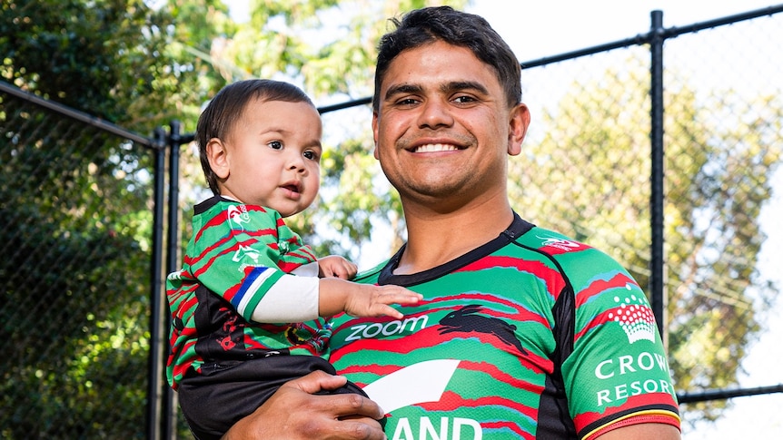 Man standing smiling at the camera while holding his baby 