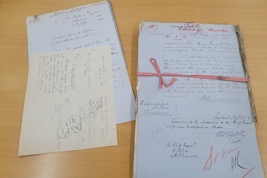 a bundle of stacked old papers tied with a red ribbon with red writing saying Cook murder