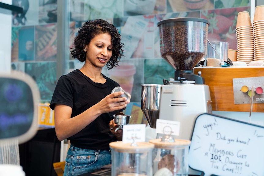 A woman stands at a coffee machine inside a cafe.