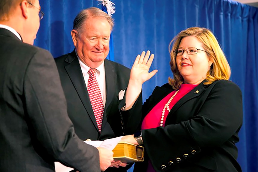 A woman holds one hand in the air with another on a bible held by a man while a second man stands next to her.