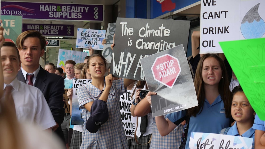 Teenagers wearing school uniforms gathered on a street holding pro-climate action signs.
