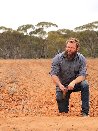 Indigenous farmer, Dominic Smith, bent on one knee in the dirt on his property in Monash.