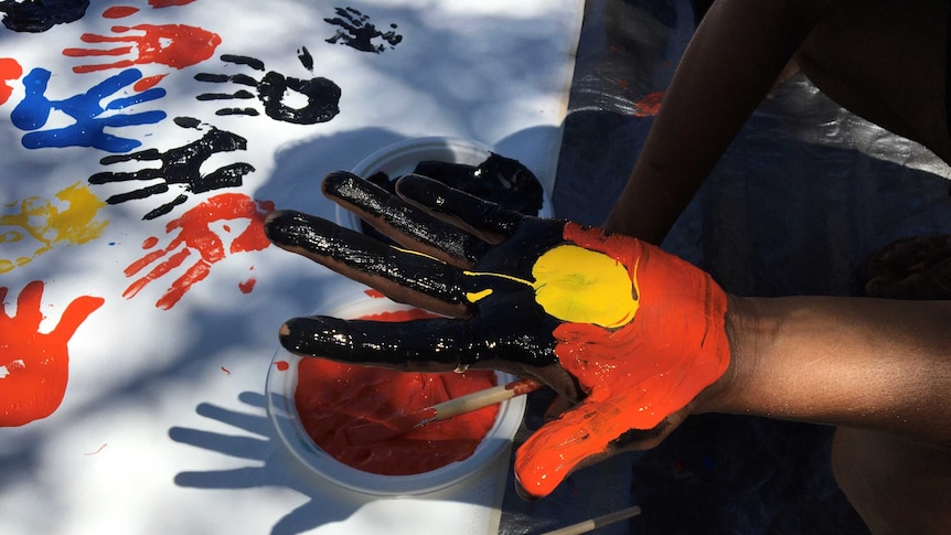 A child's hand painted with the Aboriginal flag