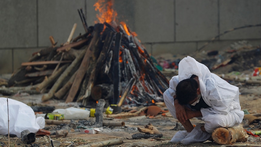 A man crouches down and hangs his head as a fire burns behind him.