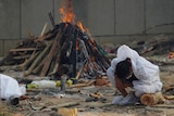 A man crouches down and hangs his head as a fire burns behind him.