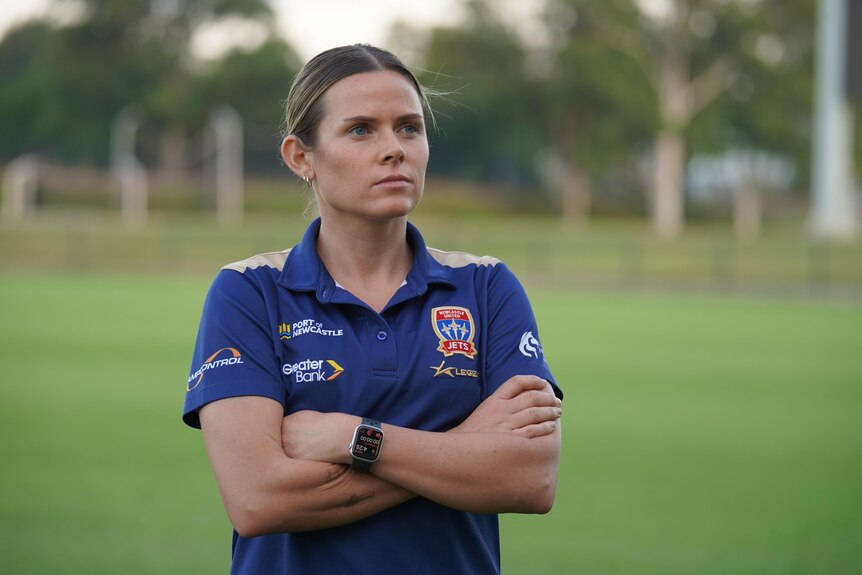 a woman, professional soccer player Cass Davis, stands with her arms crossed looking away from the camera.