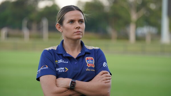 A female soccer player stands on an oval with her arms crossed.