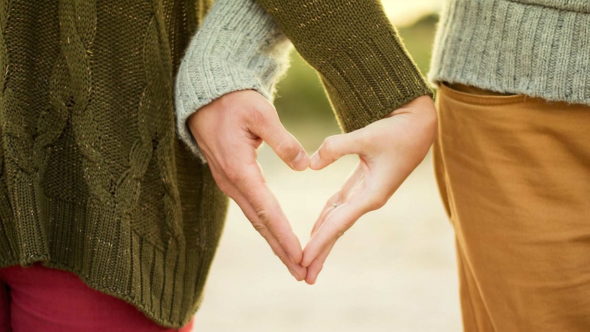 Two people make a heart symbol with their hands.