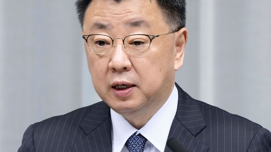 An Asian man wearing spectacles and a suit and tie, speaks during a press conference 