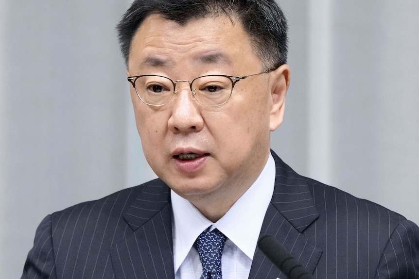 An Asian man wearing spectacles and a suit and tie, speaks during a press conference 