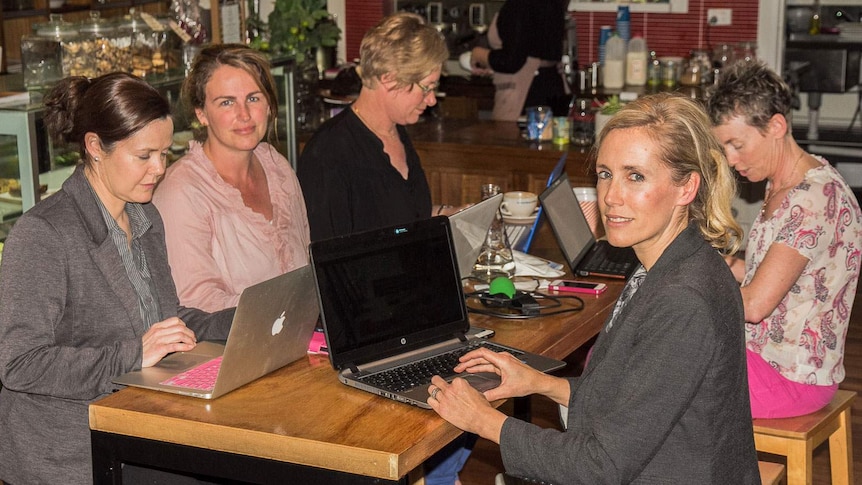 Women in a cafe sit around laptops as they develop a school fundraising app at Orange, NSW