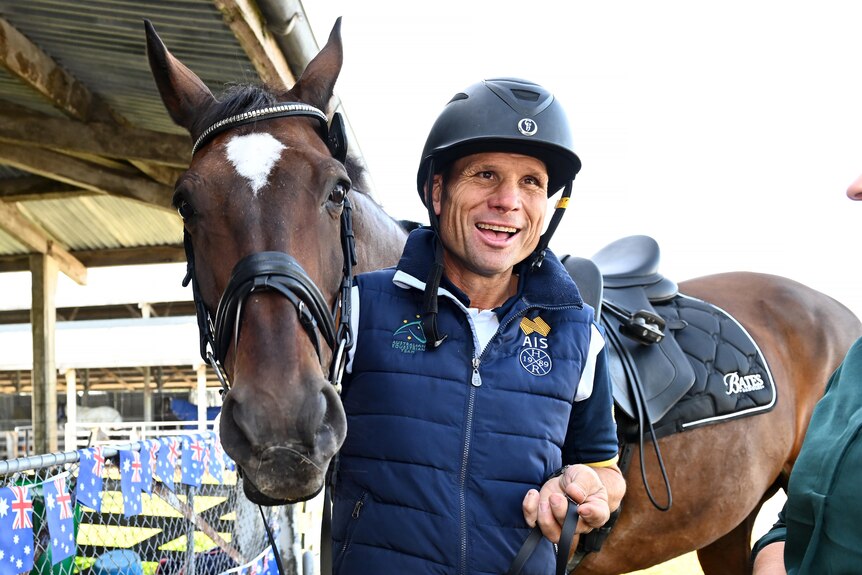 Shane Rose wears an equestrian helmet while standing with his horse Virgil.