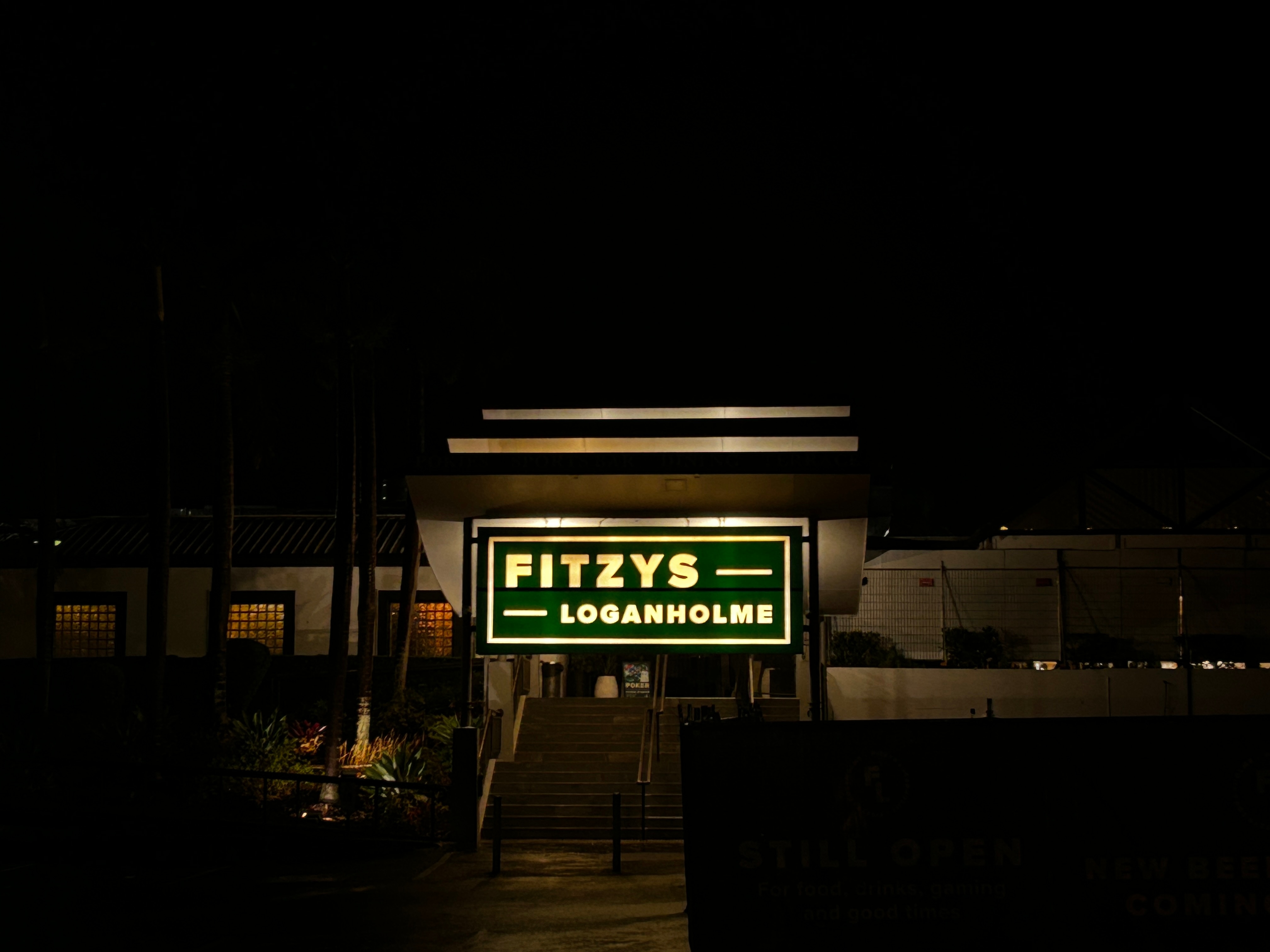 A building with an illuminated sign reading "FITZYS LOGANHOLME"viewed in the dark.