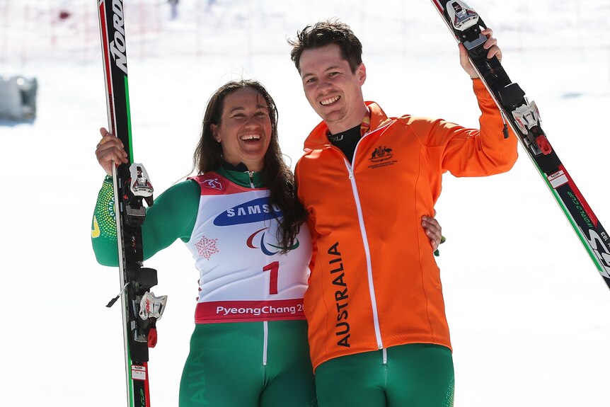 Melissa Perrine et son guide Christian Geiger tiennent un ski dans un bras et s'embrassent de l'autre en souriant à la caméra.