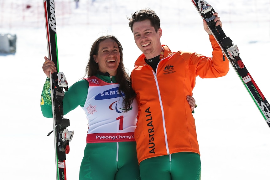 Melissa Perrine and her guide Christian Geiger hold a ski in one arm and embrace with the other, smiling at the camera.