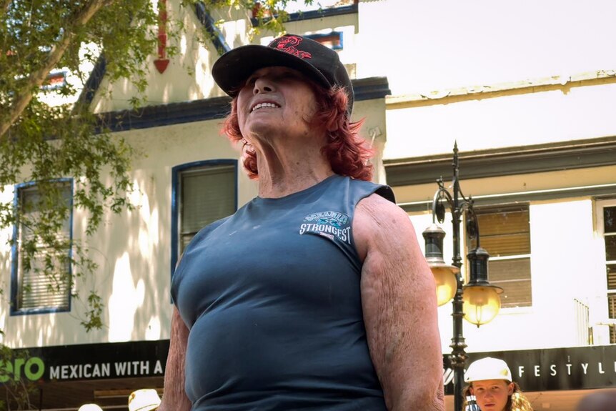 Woman in grey t-shirt with a grimace of effort on her face, lifting a 80kg weight.