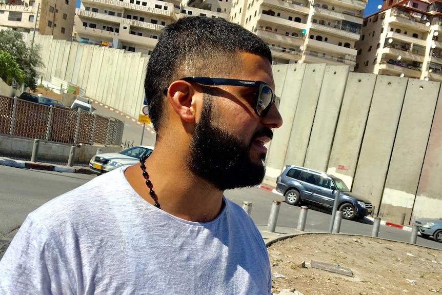 Palestinian man Yaseen, 26, walks close to a tall concrete barrier at Shuafat on the West Bank.