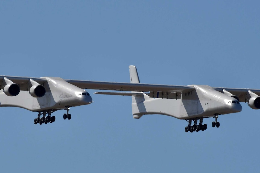 A large six-engine aircraft flies through a cloudless blue sky