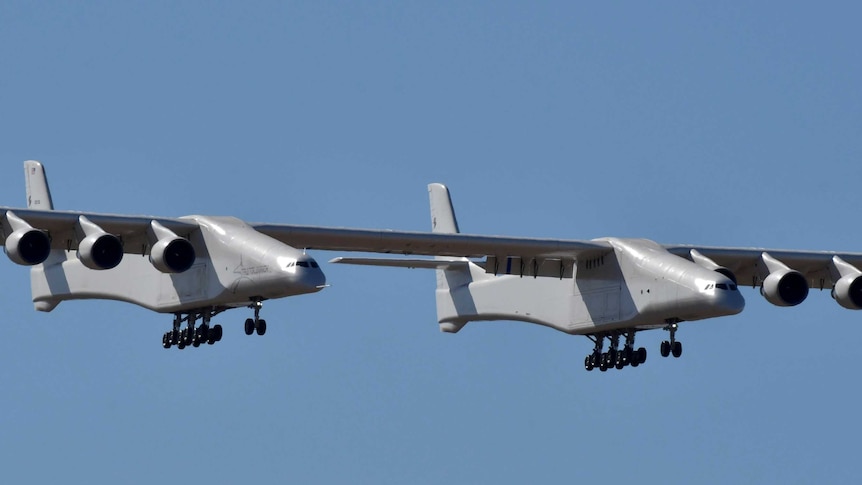 A large six-engine aircraft flies through a cloudless blue sky