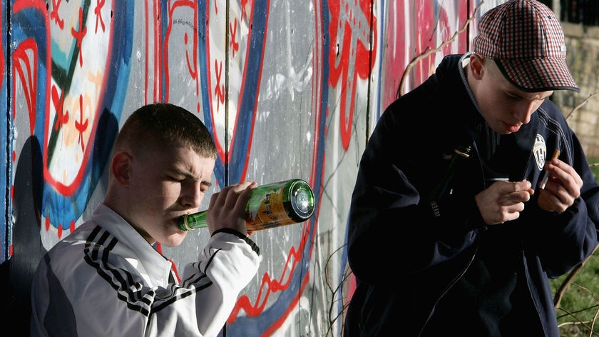 Young people stand by a wall, drinking and smoking