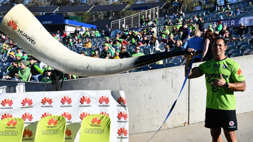 A footballer gives a thumbs up next to a giant, curved horn.