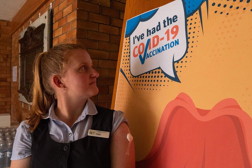 A nurse with a band aid on her arm looks at a sign that reads 'I've had the COVID-19 VACCINATION