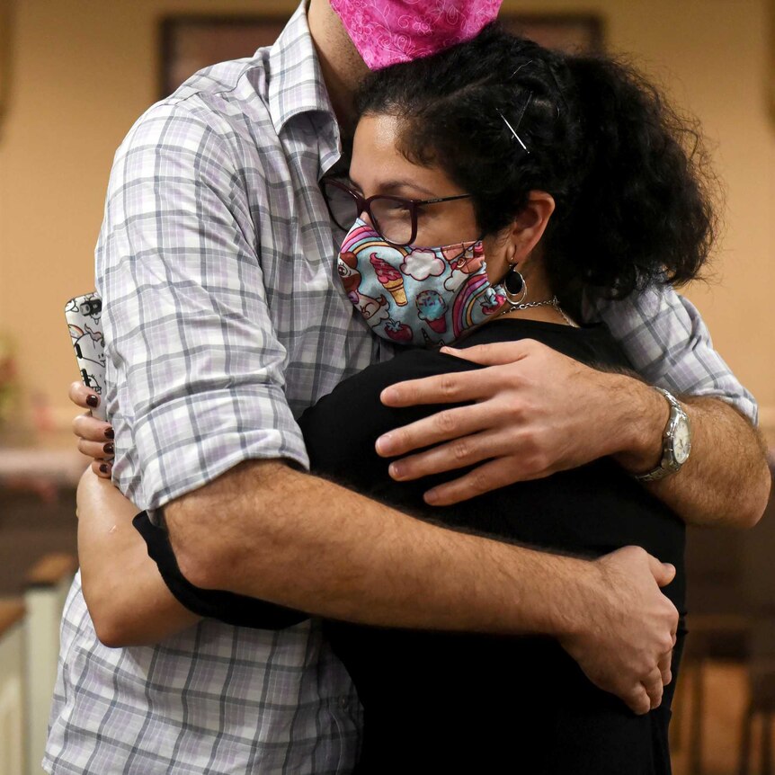 A woman in a face mask is wrapped in a big hug