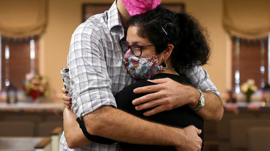 A woman in a face mask is wrapped in a big hug
