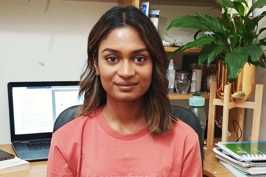 A woman sits at a desk smiling at the camera