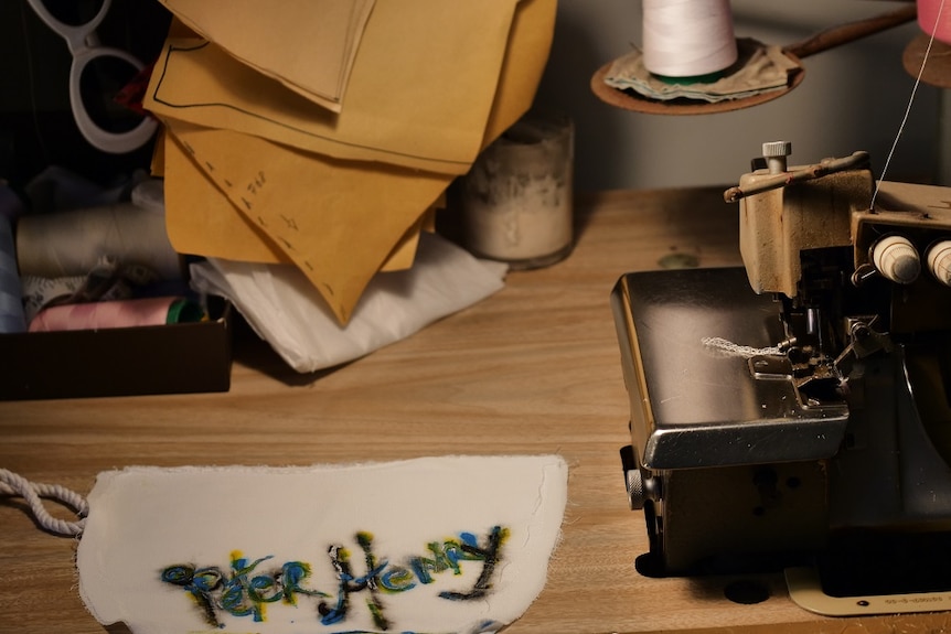 A sewing machine on a table in dim lighting with a piece of fabric titled Peter Henry in bright colours