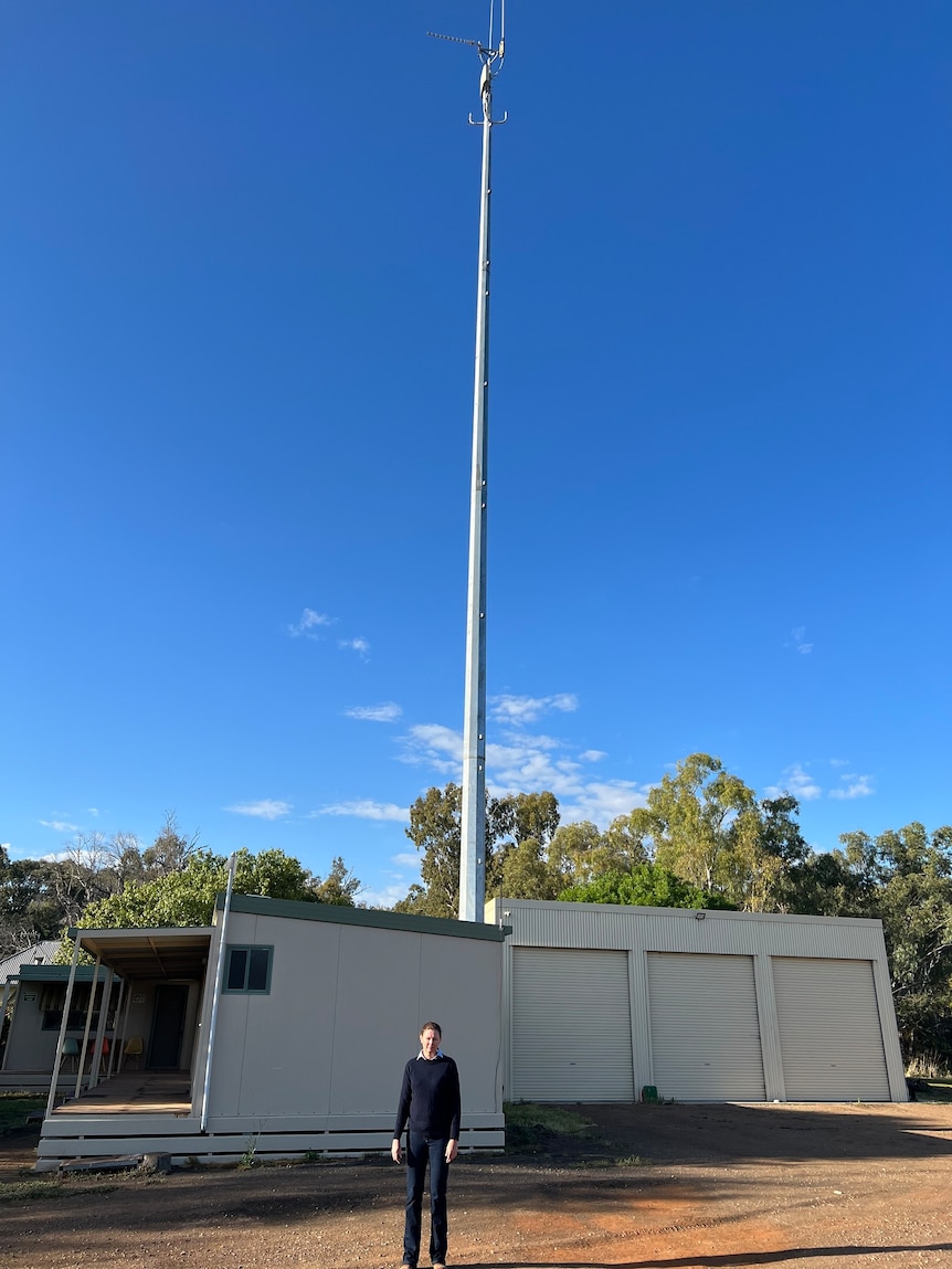 A farmer standing in front of telecommunications tower at a homestead. 