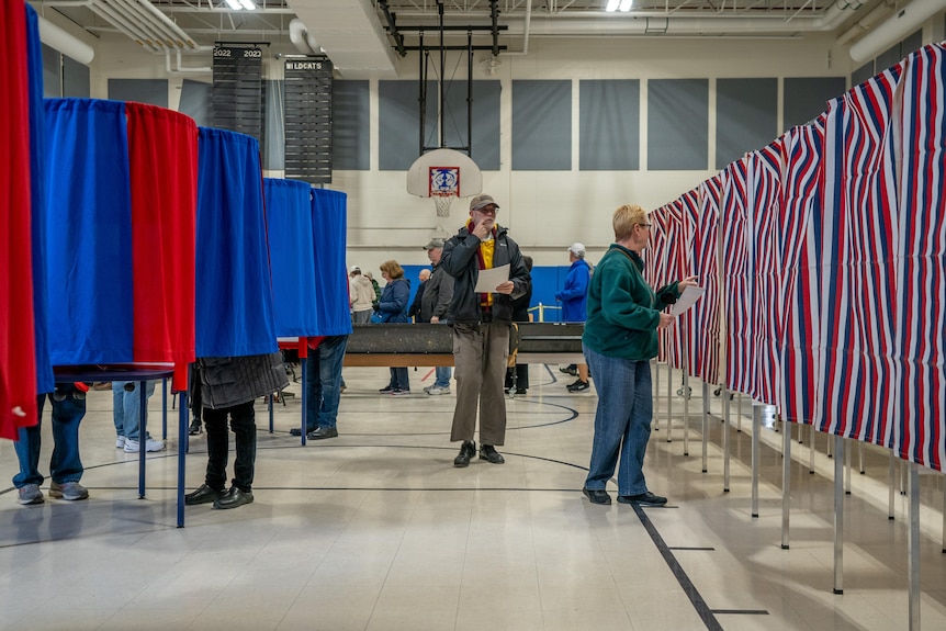 People walk between polling booths surrounded by red, white and blue curtains.