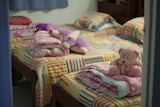 Three children's beds with folded blankets and soft toys at the foot of each bed