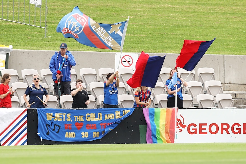 Fans of a women's soccer team hold red and blue banners and flags during a game