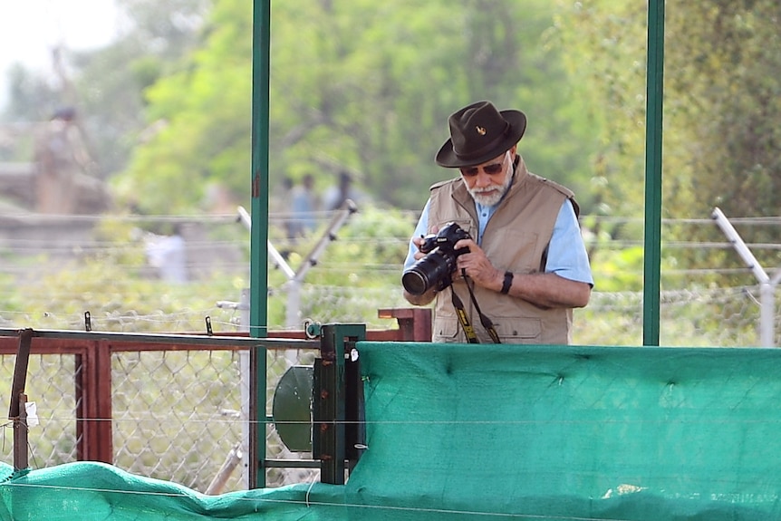Indian Prime Minister Modi holds a camera and looks down at a released cheetah.