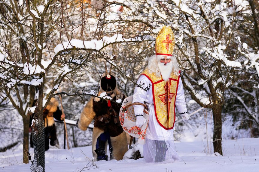 People dressed in costumes walk through the snow.