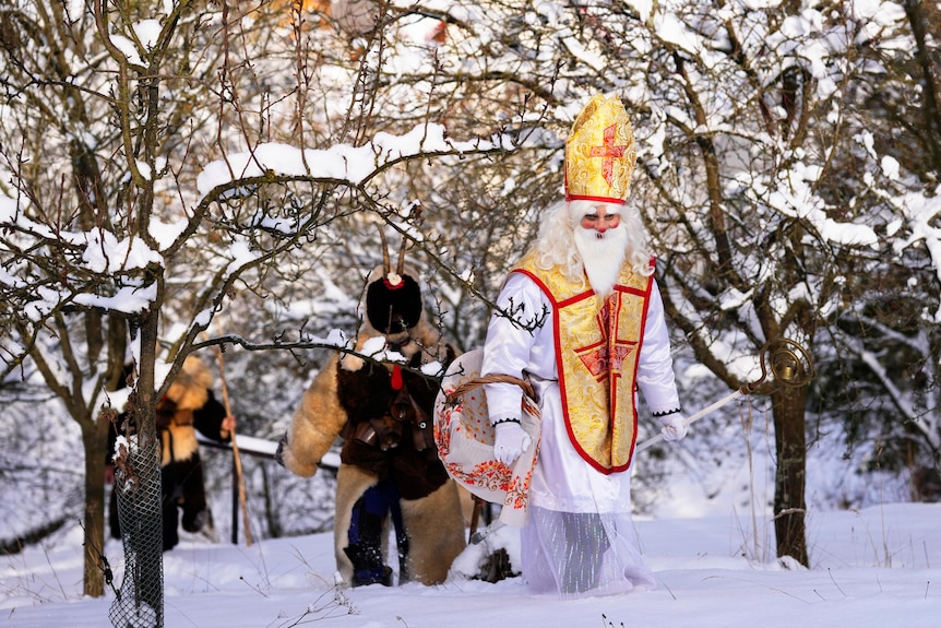 People dressed in costumes walk through the snow.