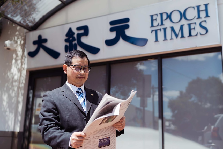 A man in a suit reads a newspaper outside the Epoch Times office.