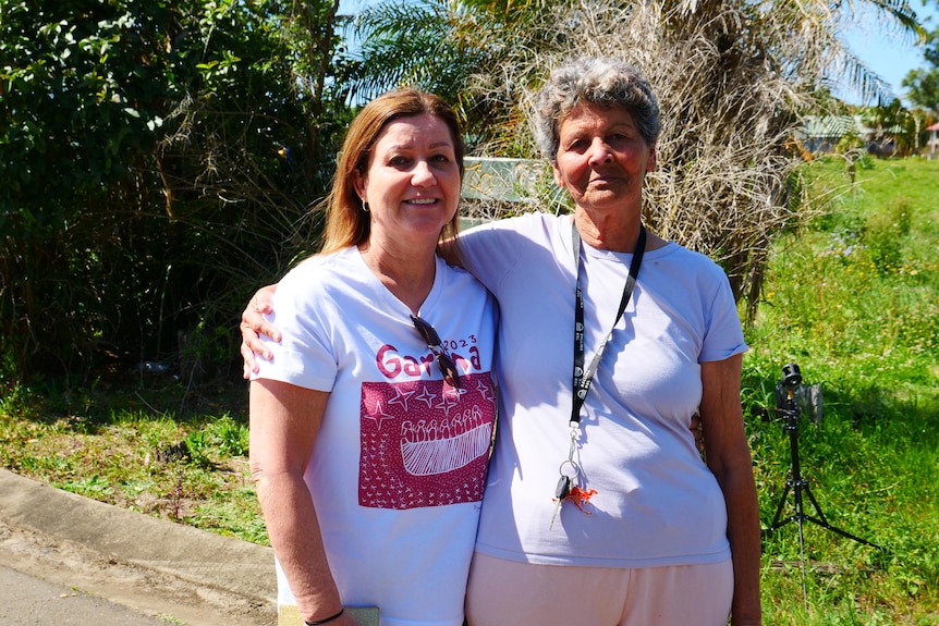 Two women standing in a street with a green paddock behind them.