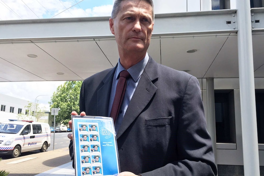 Chantelle Newbery's lawyer Robert Burns holding stamps with Newbery's face on them.