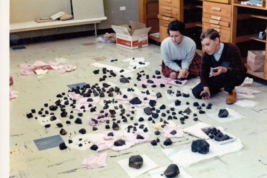 A boy and a woman squat next to fragments of rock spread out on a post office floor.