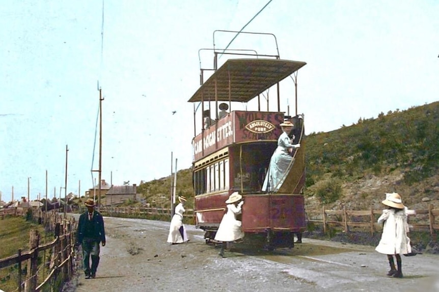 Women in long white dressed step onto a tram