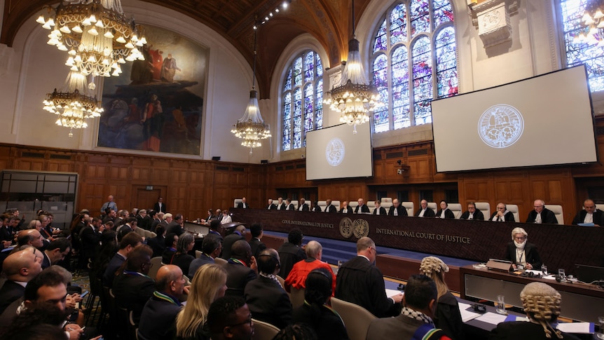 A group of people sit facing a court in a large, high-ceilinged historical building.