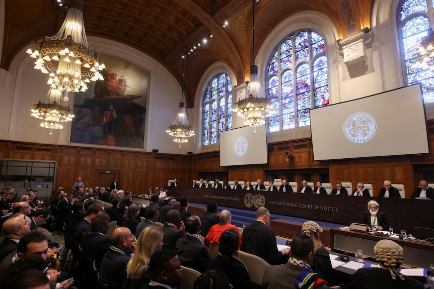 A group of people sit facing a court in a large high cielinged historical building 