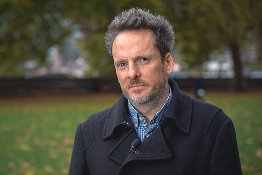 Dominic King, senior principal at Accenture Research stands in a park with grass and trees behind.